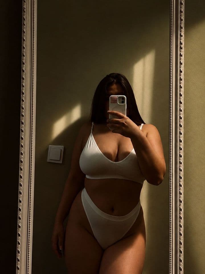 Natürliche Masseurin Diana mit weichen Kurven im weißen Dessous beim Spiegel-Selfie – Erotikmassage Berlin.